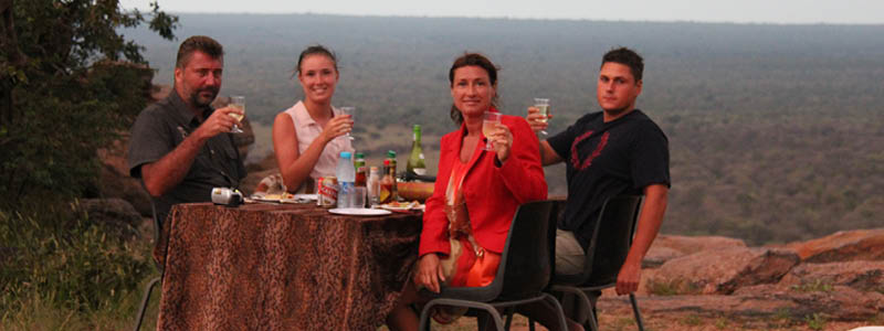 Vänner som skålar med afrikanskt vin under en middag i bushen.